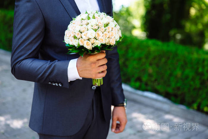 剪裁框架的特写镜头是一个温柔的玫瑰花束在新郎的手中.