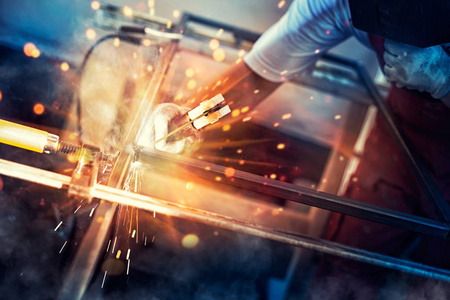 一名持有建筑手套和焊接面罩的男性焊工正在热情地工作，并在车间与焊接机金属焊接。
