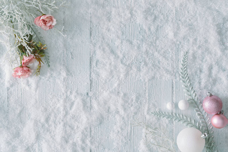 白色木制桌子背景，雪和玫瑰与树枝和圣诞球装饰。 创意冬季顶部景观