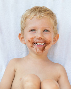 美丽的头发男孩的肖像，脸上带着巧克力，被孤立在白色背景上，男孩微笑着