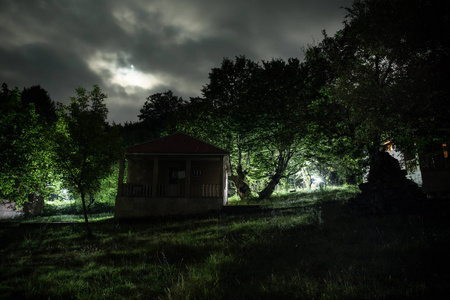 夜晚用月亮或老式乡村住宅在森林中建造的山夜景观，夜晚用云彩和星星。 夏夜。 长时间曝光拍摄的照片