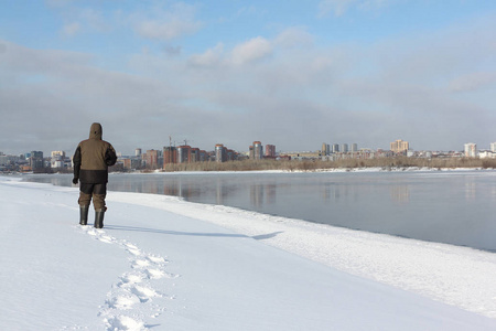 穿着暖和的衣服的高个子男人沿着冰冻的俄罗斯ob河的雪岸散步