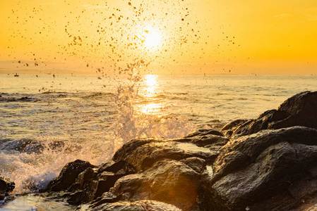 早晨的黎明在海滨的海浪拍打着岩石，溅起水来迎着太阳