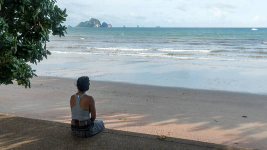 坐在海滩人行道上看岛屿的女人