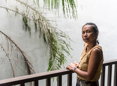 亚洲女人站在阳台上，身后有白色的墙和树