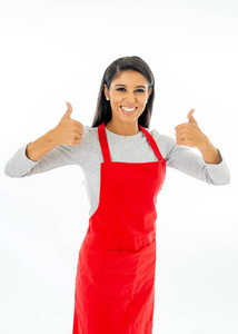 一位快乐自豪美丽的拉丁女人，穿着红色围裙，学习烹饪，在烹饪课上做拇指手势，小企业和自制的西班牙食品概念，孤立于白色之上