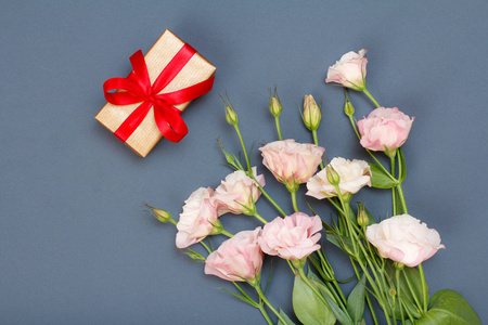 带叶子的粉红色花束和灰色背景上带红色丝带的礼品盒。 上面的风景。 庆祝日的概念。