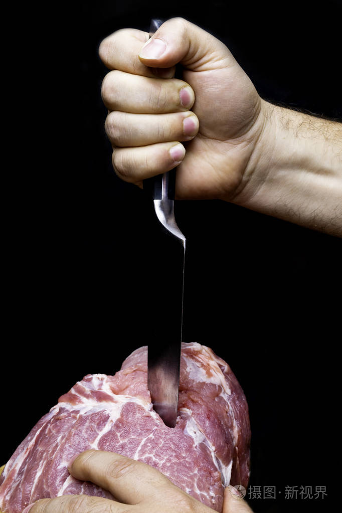 男人手里拿着刀把猪肩生切块隔离在黑色上