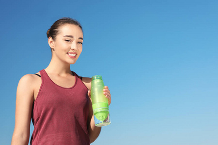 阳光明媚的日子里，年轻的运动女人拿着一瓶水对着蓝天。 文本空间