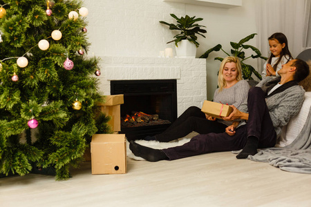 有礼物的家庭坐在客厅圣诞树附近的地板上