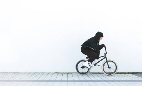 穿休闲服装的BMX骑手在白色墙壁的背景上骑自行车。 BMX概念。 bmx的街头自由泳