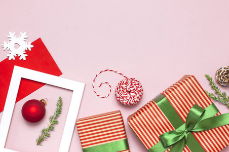 圣诞作文。 白色相框，红包，冷杉树枝，锥球，麻绳，赠送木制玩具，粉红色背景，平躺顶部视图。 圣诞节冬季装饰新年节日