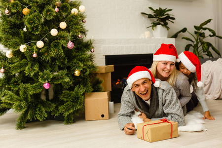 一家人戴着红色圣诞帽，礼物躺在客厅圣诞树附近的地板上