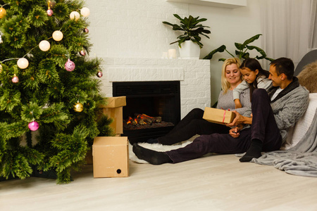 有礼物的家庭坐在客厅圣诞树附近的地板上