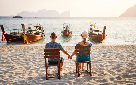 年轻夫妇坐在泰国南部PhiPhi岛热带海滩上的椅子上。 旅游杂志的概念。