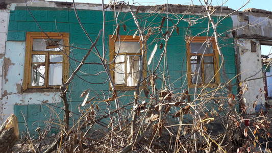 砸碎玻璃窗与旧木框架上的粗糙墙壁损坏的房子。旧的废弃建筑。废弃建筑的正面