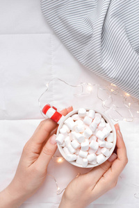 新年或圣诞节平躺在顶部，上面有热可可咖啡巧克力和棉花糖杯在女人手中，圣诞节庆祝活动在床上与灯光。 概念博客社交媒体2019