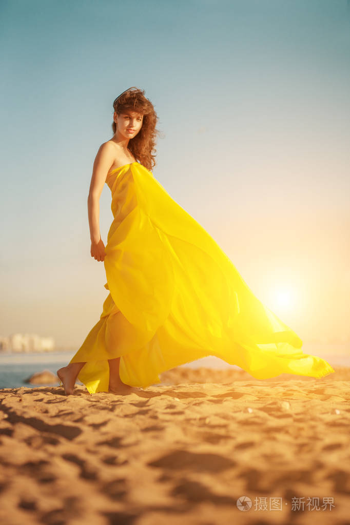 穿着长裙的时尚女孩在夏天日落的背景下.