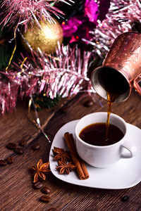 把咖啡从Jezve倒进圣诞树下的杯子里。 乡村风格
