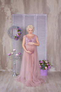 怀孕母亲和幸福未来母亲的概念孕妇穿着紫罗兰色的裙子，花束在五颜六色的墙上，摆着银色的烛台。