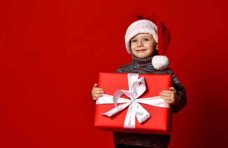 滑稽的微笑快乐的孩子男孩在圣诞老人帽子拿着圣诞礼物礼物在手