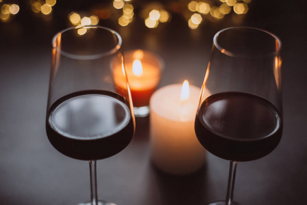 一张黑桌子上摆着两杯红酒，上面有蜡烛和花环