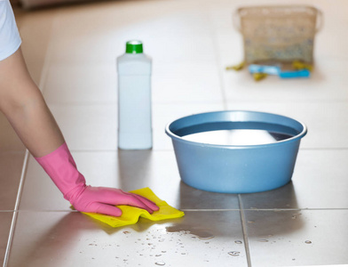 家务和家务观念密切妇女在橡胶手套与布和洗涤剂喷雾清洁地板在家里。