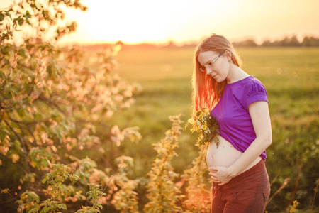 日落和自然背景下的孕妇。 美丽的年轻女孩模特，肚子在阳光下背光。