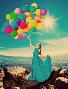 奢华时尚时尚的女人，手拿气球在海滩上对抗天空和太阳穿着长裙