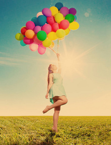 豪华时尚女性，手拿气球在田野上，对着天空和太阳。