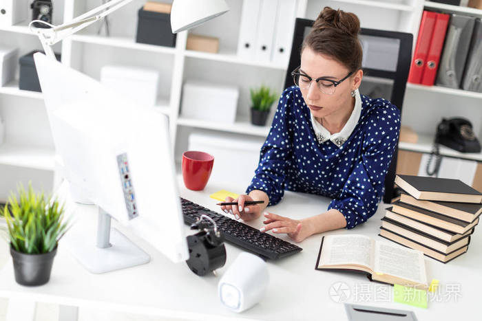 一个戴眼镜的年轻女孩坐在办公室的桌子上, 在键盘上打印