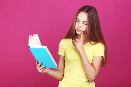 年轻女孩拿着粉红色背景的书