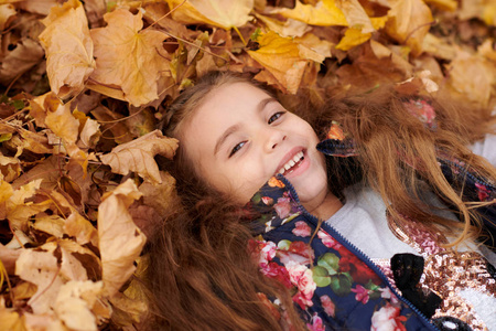 女孩子在秋天的城市公园里躺在落叶里玩。