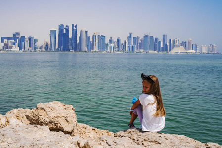 小女孩坐在康尼卡百老汇，看多哈天际线的景色。 卡塔尔。
