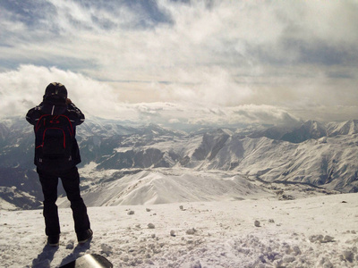 人站在山顶，俯瞰雪山景观，冬季旅行和冒险理念。 山顶上的滑雪者。 极限运动。 徒步旅行和徒步旅行的背景。 动机概念