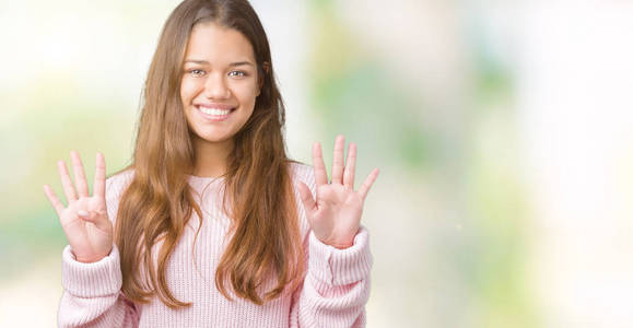 年轻漂亮的黑发女人穿着粉红色的冬季毛衣，在孤立的背景上，用手指数字9，同时微笑着自信和快乐。
