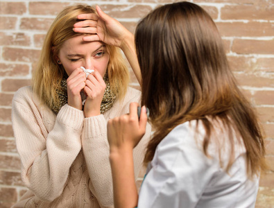 女人打喷嚏感到很不舒服。戴围巾的女孩在医生检查她的时候拿着纸巾。识别感冒症状。补救措施应该有助于快速战胜寒冷。感冒和流感的治疗方