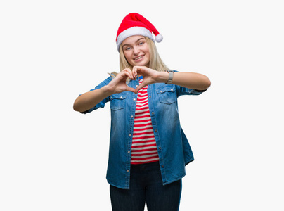 年轻的高加索女人戴着圣诞帽，在孤立的背景上微笑，在爱中显示出心脏的象征和形状，用手。 浪漫的概念。