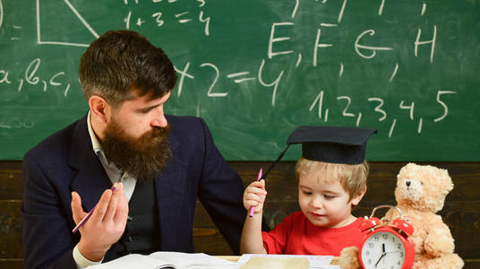 父亲教儿子数学。老师在正式的穿着和学生在砂浆板在教室里, 黑板在背景上。算术课概念。快乐的孩子学习与老师
