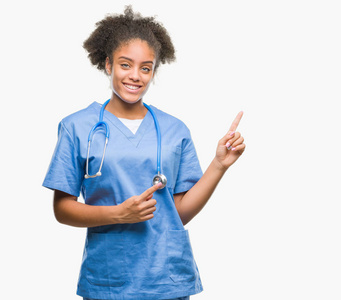 年轻的非洲美国医生女士在孤立的背景上微笑，看着相机，用两只手和手指指向一边。