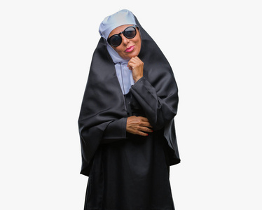 中年天主教修女，戴着太阳镜，在孤立的背景上，手在下巴上思考问题，沉思的表情。 带着体贴的脸微笑。 怀疑概念。