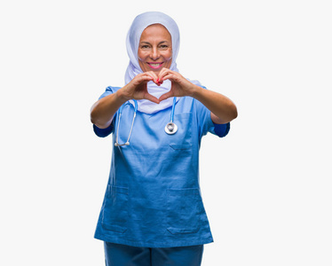 中年阿拉伯护士女士戴着头巾，在孤立的背景上微笑，在爱中显示出心脏的象征和形状，用手。 浪漫的概念。