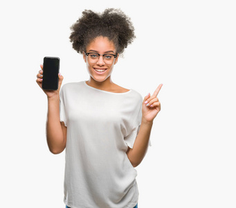年轻美丽的AFRO美国显示智能手机屏幕上孤立的背景，非常高兴地用手和手指指向一边。