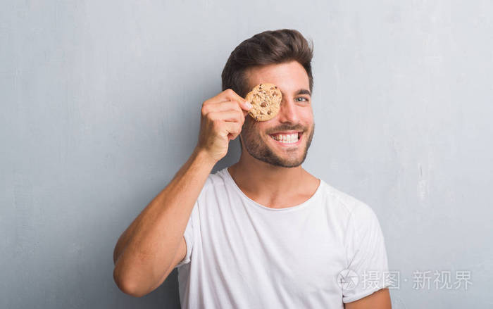 一个英俊的年轻人穿着灰色的格子墙吃着巧克力饼干脸上挂着快乐的表情