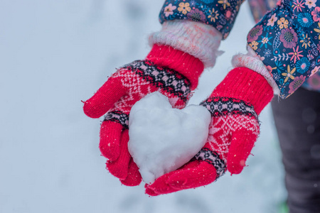 雪心在女孩手中。 双手穿着针织手套，捧着雪做的红心。