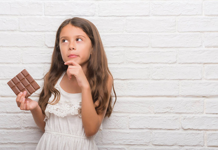 年轻的西班牙裔小孩在白砖墙上吃巧克力棒，严肃的脸，思考问题，非常困惑的想法