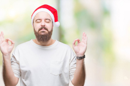 年轻的白种人嬉皮士戴着圣诞帽在孤立的背景下放松和微笑，闭着眼睛做冥想手势用手指。瑜伽概念。
