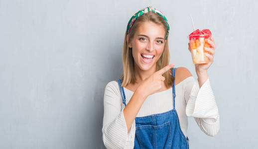 美丽的年轻女子在灰色的墙壁上吃水果，非常高兴地用手和手指指着。