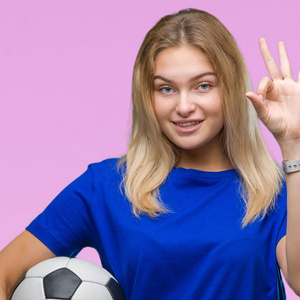 年轻的白种人女子在孤立的背景下拿着足球，用手指做着好的标志，很好的象征