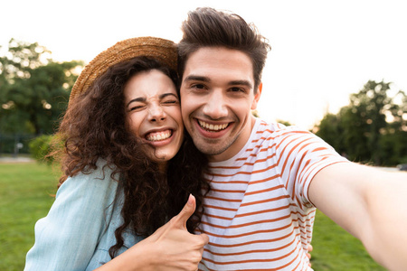 20多岁的可爱情侣在绿色公园散步，在手机上自拍